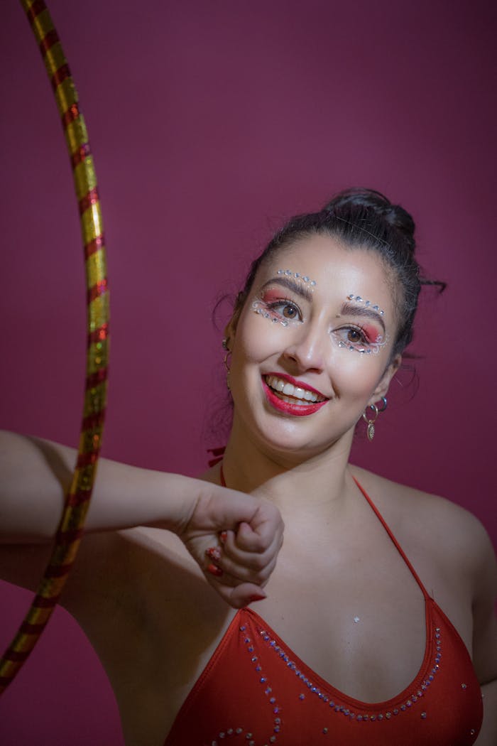 classes-03 Smiling woman in a red outfit with artistic makeup holding a hula hoop against a vibrant background.