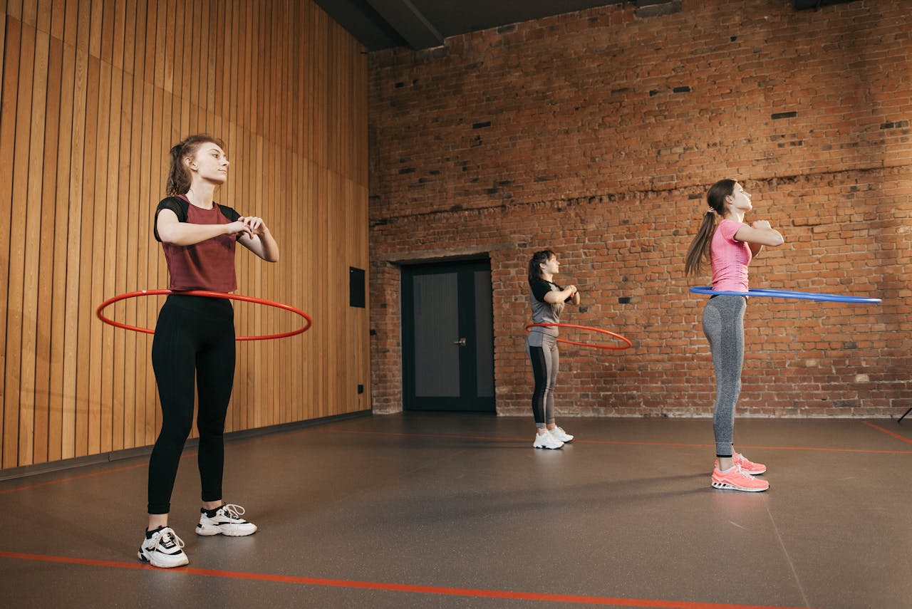 about-img Three women using hula hoops in an indoor gym setting, focusing on fitness.